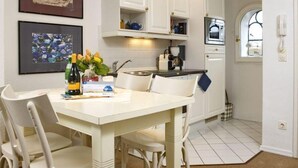A kitchen with white cabinets, a dining table with chairs, and a window with a view of the beach. - Old town gate in Friesenpark, apartment 7 (Sylt)