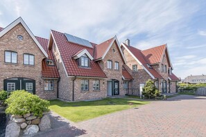 A row of brick houses with red-tiled roofs and green lawns.