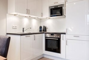 A modern kitchen with white cabinetry, a built-in oven, a microwave, and a coffee maker.