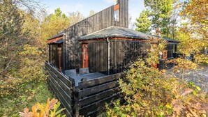 A rustic cabin with a wooden exterior, a chimney, and a porch area surrounded by autumn foliage.