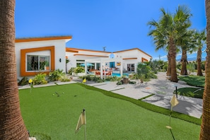 A modern house with a pool, a well-maintained lawn, and palm trees. - PS Playground - Putt Chip - Horseshoe - Corn Hole - Pool Table (Palm Springs)
