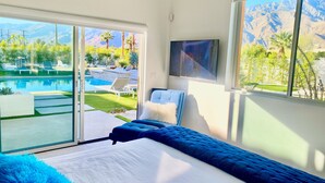 A bedroom with a bed, a TV, and a view of a pool and mountains. - PS Playground - Putt Chip - Horseshoe - Corn Hole - Pool Table (Palm Springs)