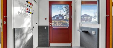 A modern hallway with a red door, a hand sanitizer dispenser, and a view of houses through the door.
