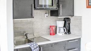 A compact kitchenette with a microwave, coffee maker, and a red telephone.