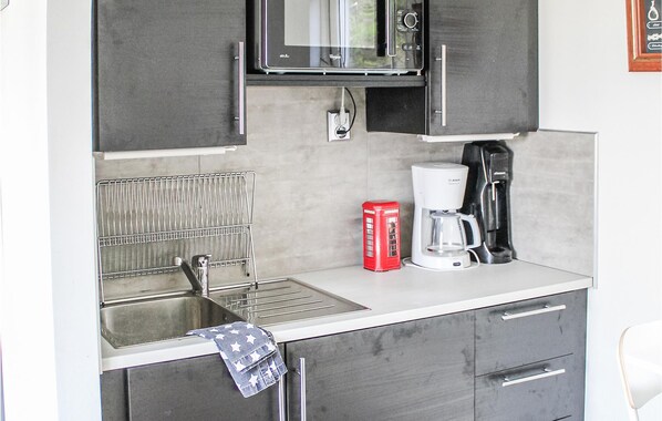 A compact kitchenette with a microwave, coffee maker, and a red telephone.