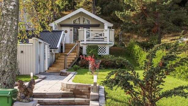 A two-story house with a front deck and a small porch. There is a wooden staircase leading to the front door.