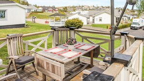 A wooden deck with a table and chairs, a potted plant, and a gazebo in the background.