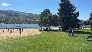 A beach volleyball game on a sunny day with a lake and hills in the background.