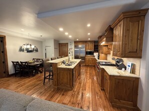 A kitchen with wooden cabinets, a granite countertop, stainless steel appliances, and a dining area with a table and chairs.