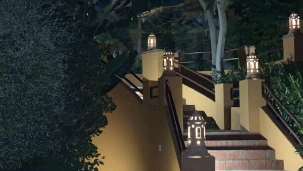Une vue nocturne d’un escalier dont les rampes sont illuminées, entouré de verdure et agrémenté d’une lanterne décorative.