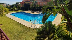 Une piscine entourée d’une pelouse bien entretenue et de palmiers, avec un bâtiment en arrière-plan.