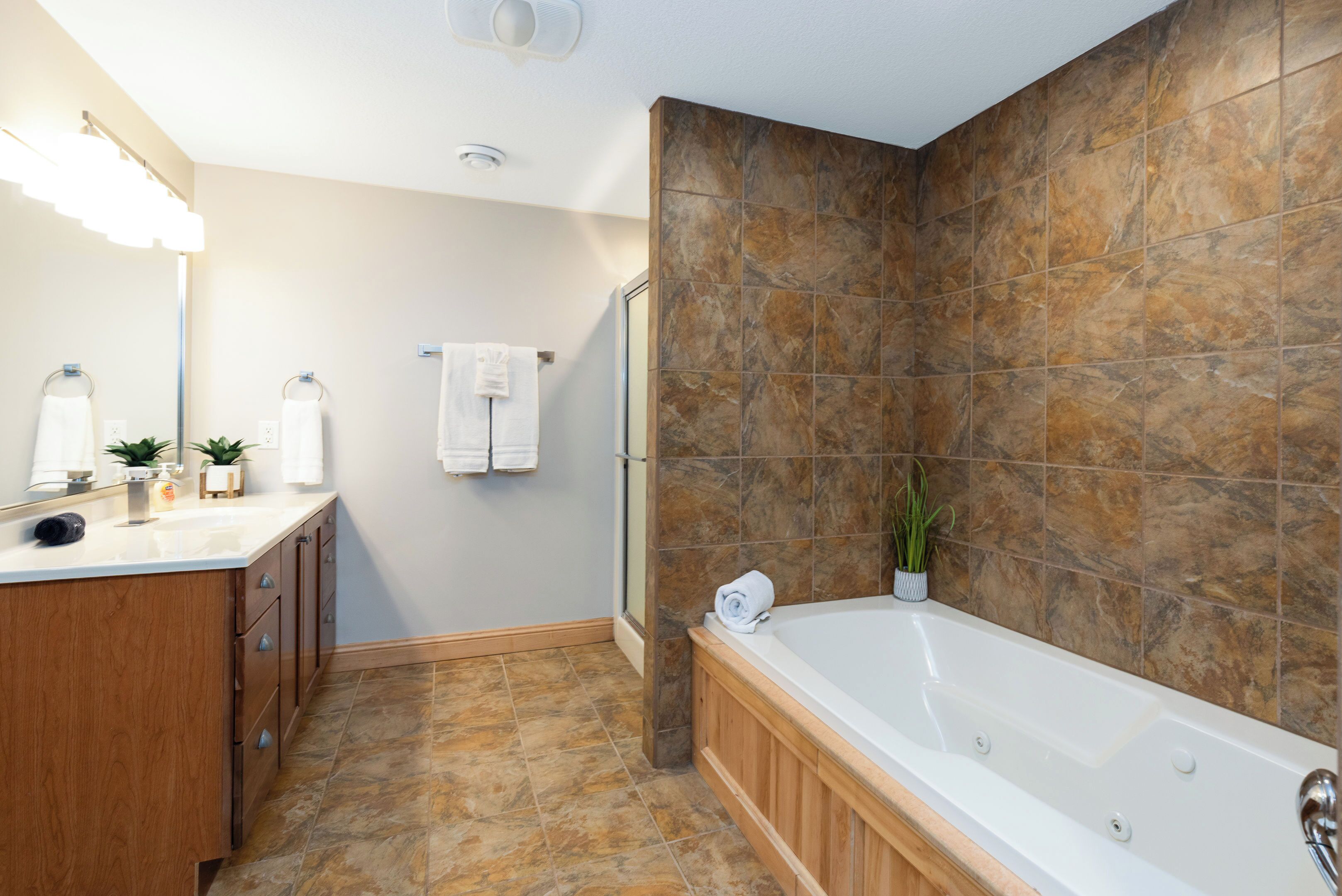 Un baño moderno con un mueble de tocador de madera, una bañera grande y una zona de ducha.