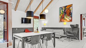 A modern dining area with a white table, grey chairs, and a red chair. There are pendant lights, a painting on the wall, and a TV above the table. - Beautiful home in Grenaa with WiFi (Grenaa)