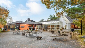 An outdoor seating area with tables and benches, a greenhouse, and a building with a sloped roof. - Beautiful home in Grenaa with WiFi (Grenaa)
