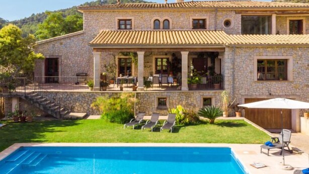 Una casa de piedra con piscina, mobiliario exterior y vistas a las colinas.