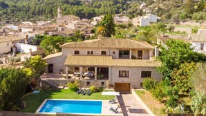 Una villa con piscina, rodeada de exuberante vegetación y un pueblo en la ladera.