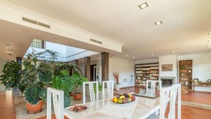 Un comedor amplio con una larga mesa, sillas blancas y una variedad de frutas y verduras sobre la mesa.