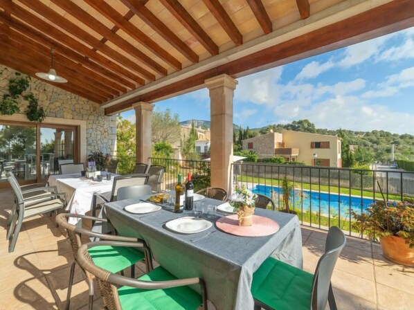 An outdoor patio with tables and chairs, overlooking a swimming pool and a scenic view of houses and hills.