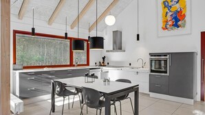 A modern kitchen with a large island, black chairs, a dining table, and a large window with a view of trees. - 2 bedroom gorgeous home in Grenaa (Grenaa)