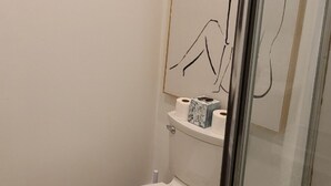 Un baño con un inodoro, un rollo de papel higiénico y una obra de arte abstracto enmarcada en la pared.