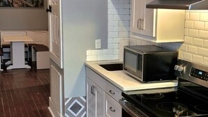 Cocina compacta con microondas, estufa y armarios blancos.