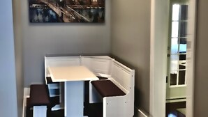 Habitación de esquina con cama blanca, una mesita y un banco.