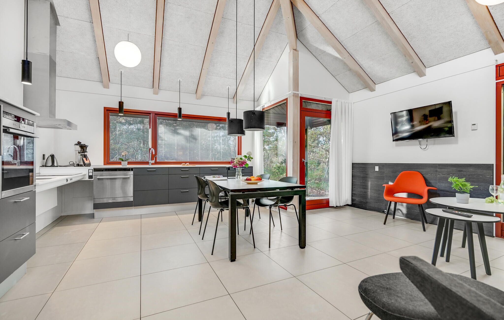 A modern kitchen with a dining area, large windows, and a TV mounted on the wall.