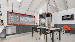 Uma cozinha moderna com área de refeições, apresentando uma grande janela, forno embutido e televisão de tela plana na parede.