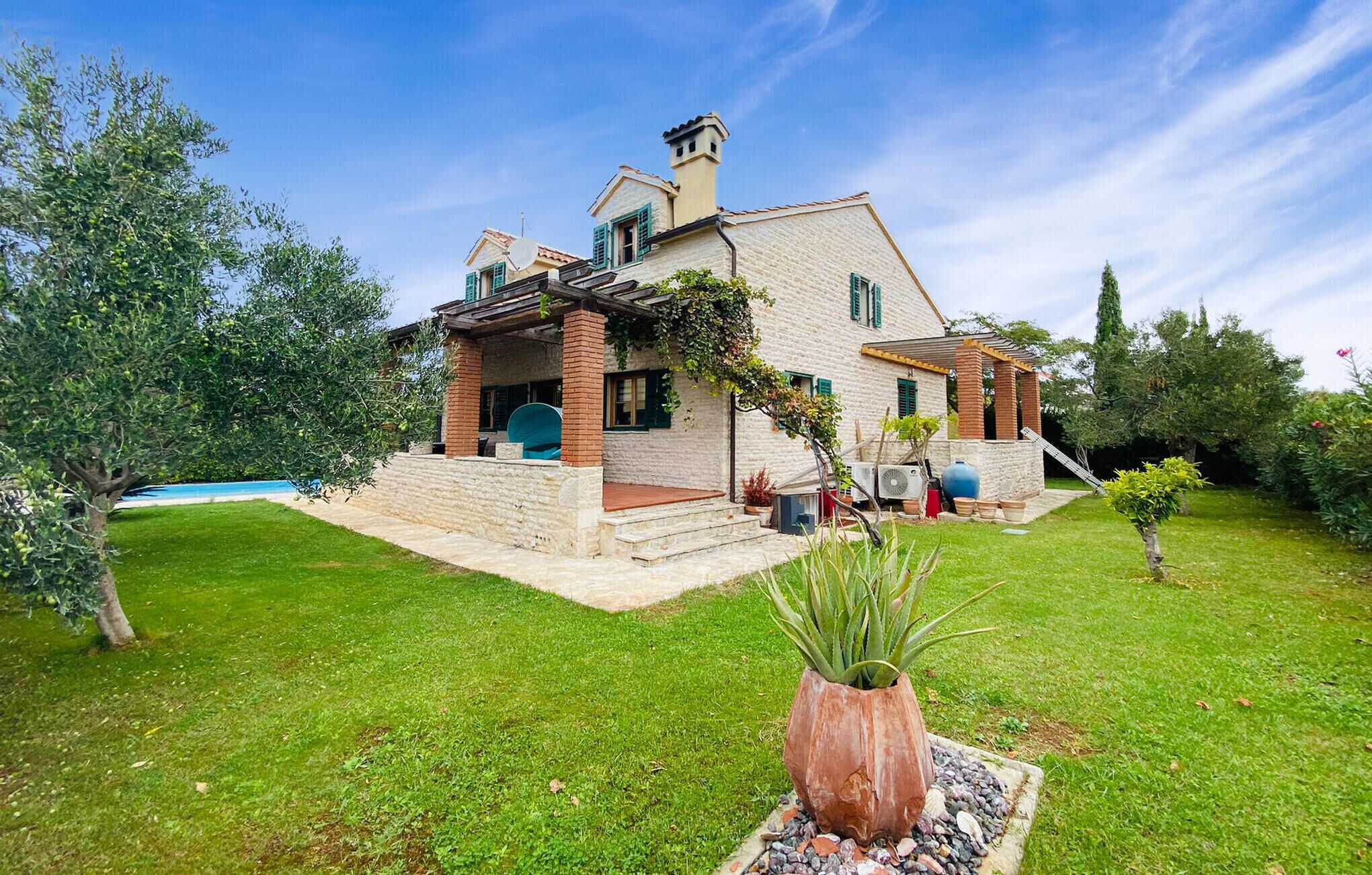 Une maison à deux étages avec une façade en pierre, une entrée en briques et un petit jardin agrémenté d’une plante en pot.