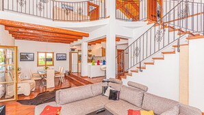 A spacious living area with a large sectional sofa, a dining table, and a kitchen in the background. A wooden staircase with a metal railing leads to an upper level. - Beautiful home in Vodice with sauna (Vodice)