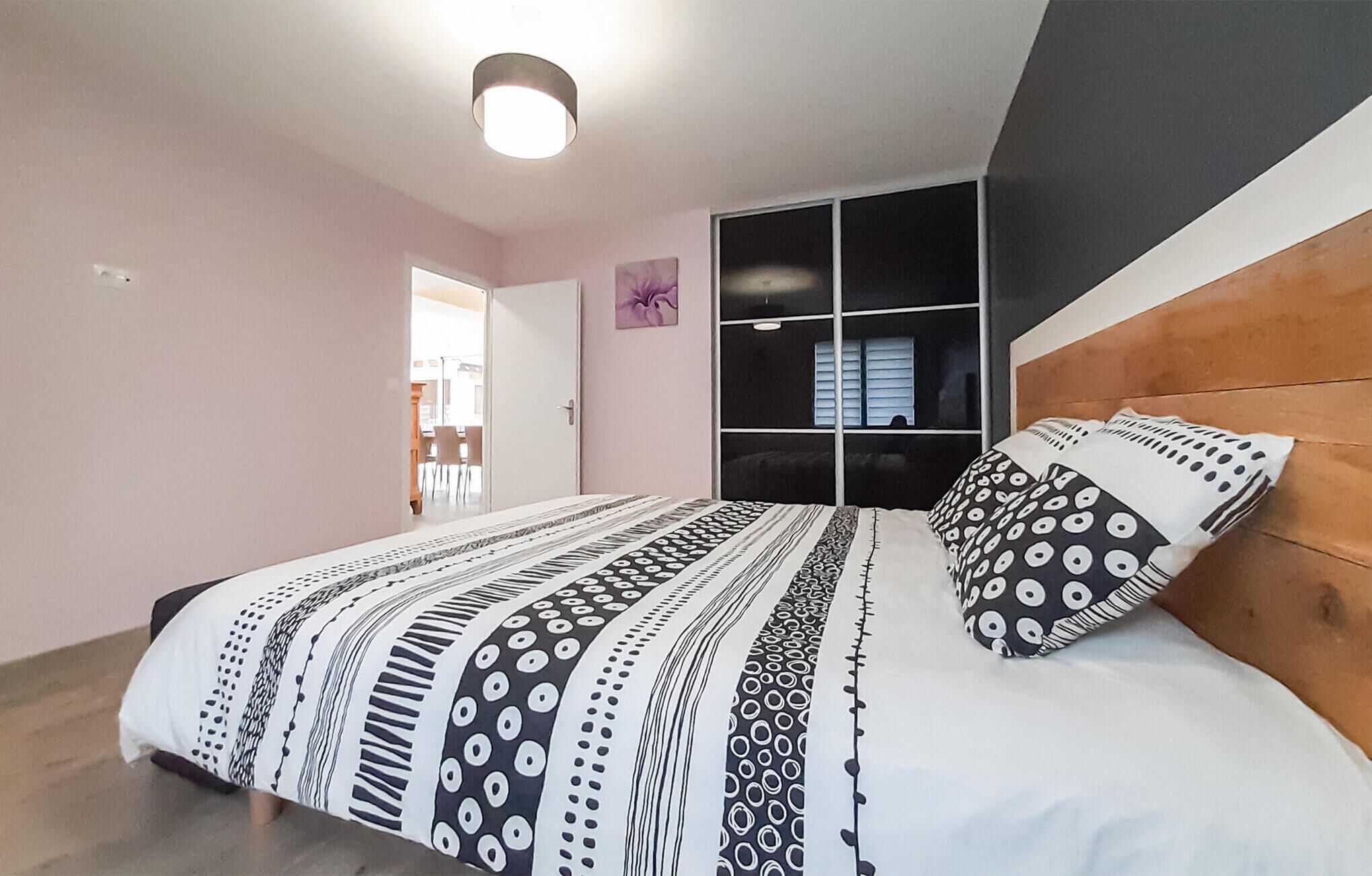 A bedroom with a bed, a wooden headboard, a wardrobe, and a ceiling light.