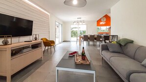 Un salon moderne doté d’un téléviseur à écran plat, d’un meuble de rangement en bois, d’un canapé gris et d’une table basse sur laquelle se trouvent une bouteille et des verres.