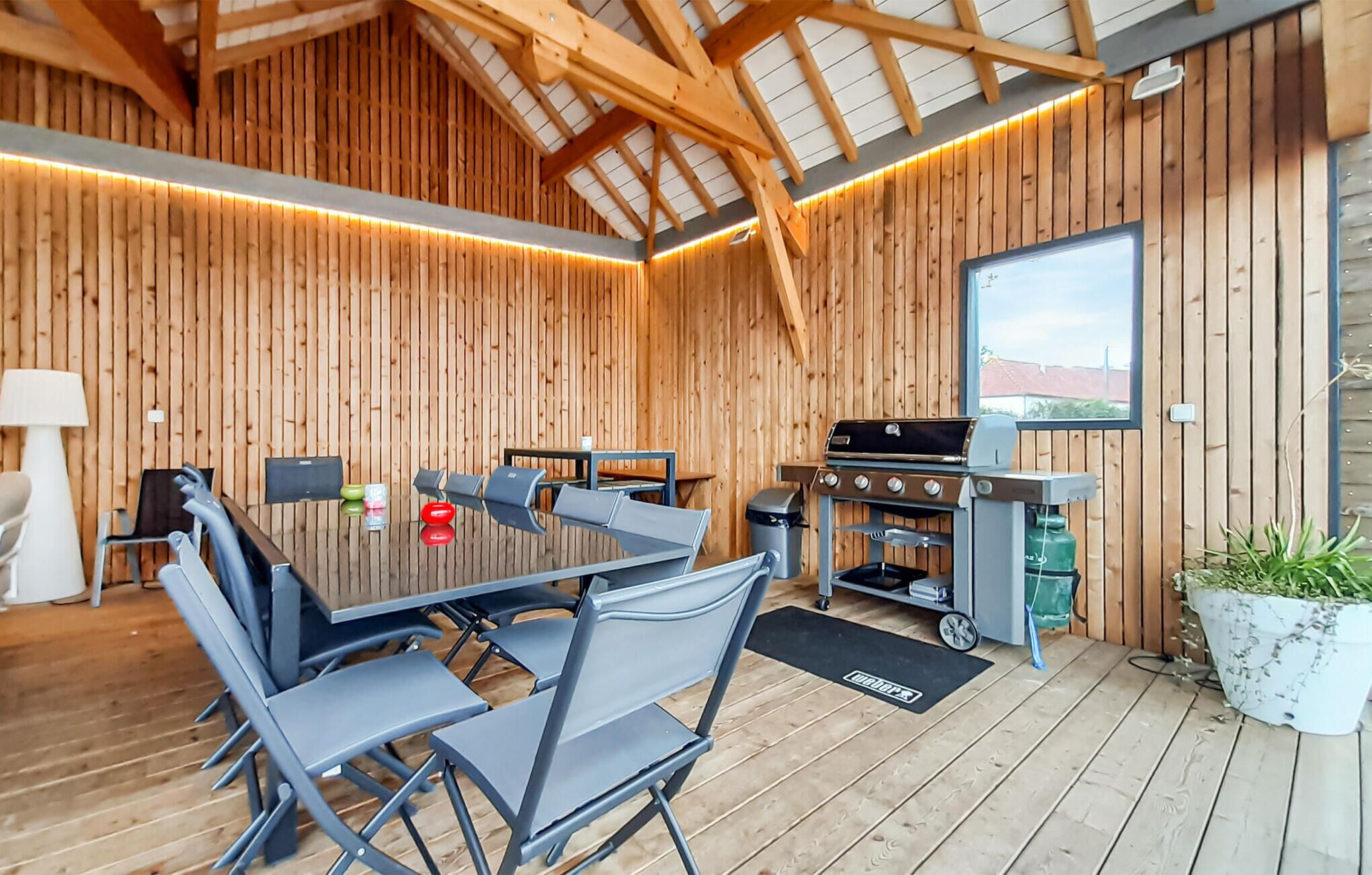 A wooden interior with a dining table, chairs, a grill, and a potted plant.