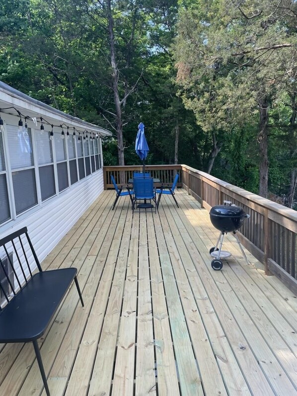 Une terrasse en bois avec une table et des chaises, un barbecue et une guirlande lumineuse.