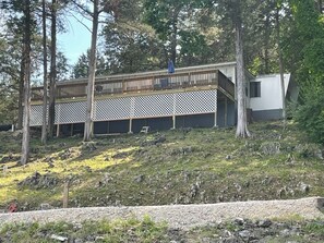 A cabin with a wooden deck, surrounded by trees and a rocky hillside.