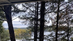 Une vue depuis une véranda couverte donnant sur un lac où sont amarrés des bateaux, le tout entouré de grands arbres.