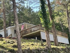 A cabin with a wooden deck and a covered porch, surrounded by trees.