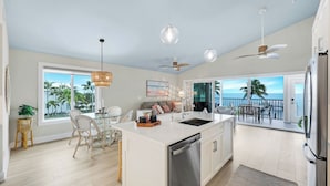 A spacious kitchen with a large island, a dining area with wicker chairs, and a balcony with a view of the ocean. - Captiva Hide A Way 2D- Luxury Captiva Condo, Everything You Need! (Captiva)