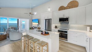 A modern kitchen with white cabinetry, a large island with bar stools, a built-in oven, and a view of the sea through large windows. - Captiva Hide A Way 2D- Luxury Captiva Condo, Everything You Need! (Captiva)