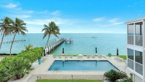 A pool with a view of the ocean, palm trees, and a pier. - Captiva Hide A Way 2D- Luxury Captiva Condo, Everything You Need! (Captiva)