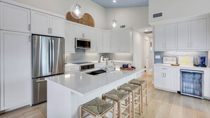 A modern kitchen with white cabinetry, stainless steel appliances, a central island with stools, and a decorative wall piece. - Captiva Hide A Way 2D- Luxury Captiva Condo, Everything You Need! (Captiva)