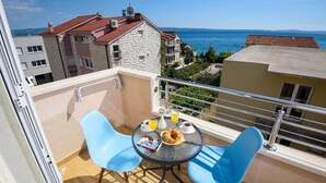 Un balcón con dos sillas azules, una mesa redonda pequeña con cosas para el desayuno, y vista al mar y edificios.