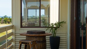 Una terraza de madera con una mesa, sillas, un ventanal grande y una planta en maceta.