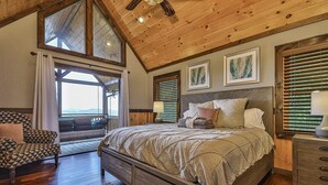 Een slaapkamer met een groot bed, houten plafond en uitzicht door een raam.