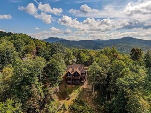 A cabin surrounded by dense forest with a clear view of distant mountains.