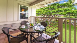 A covered outdoor dining area with a table set for four, surrounded by wicker chairs, overlooking a well-maintained lawn and trees.