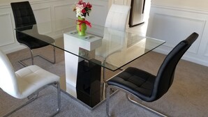Et spiseområde med et bord med glasplade, fire stole, en vase med blomster og et hvidt skab.