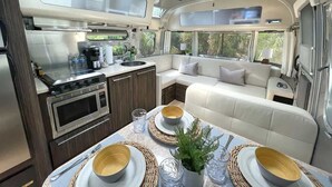 A compact RV interior with a kitchenette, dining area, and a seating area with a view of the outdoors. - Large Home w 2 Airstream Glampers & Spa near Beach & Downtown (Savannah)