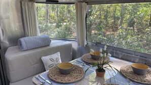 A cozy interior with a seating area and a dining table set for two, featuring woven placemats and a potted plant. - Large Home w 2 Airstream Glampers & Spa near Beach & Downtown (Savannah)