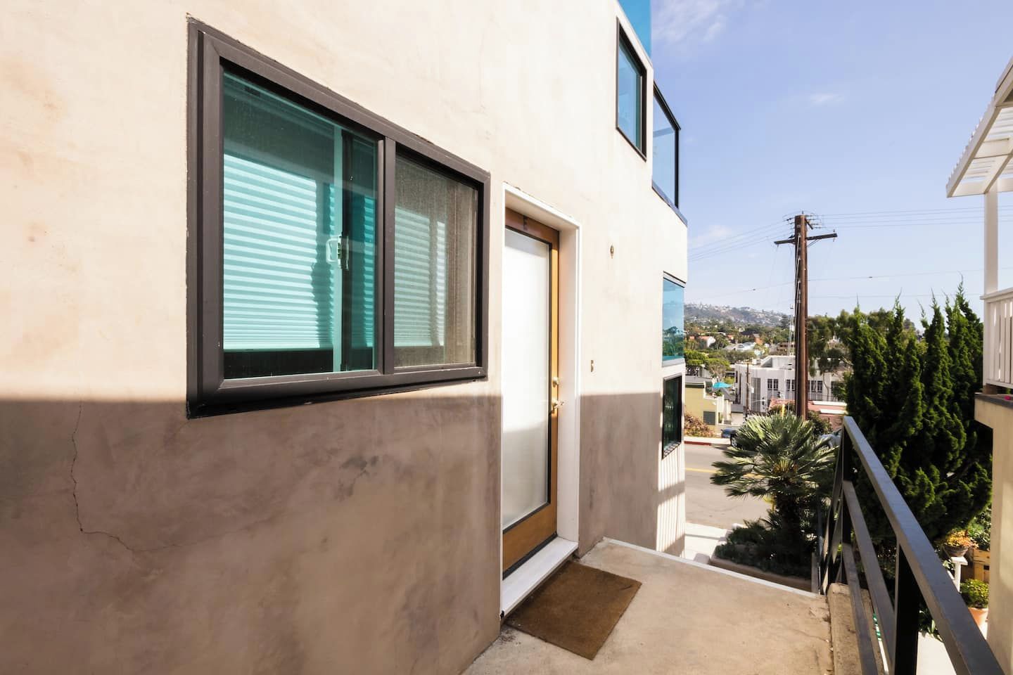 Un balcon donnant sur un quartier résidentiel, une porte et une fenêtre avec des stores.